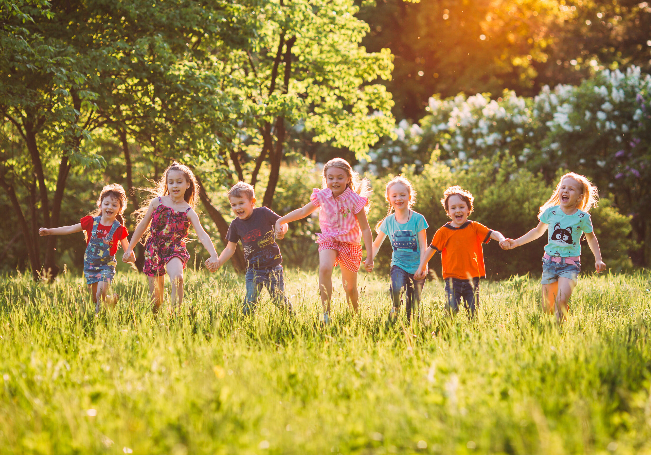 Large group of kids, friends boys and girls running in the park on sunny summer day in casual clothes